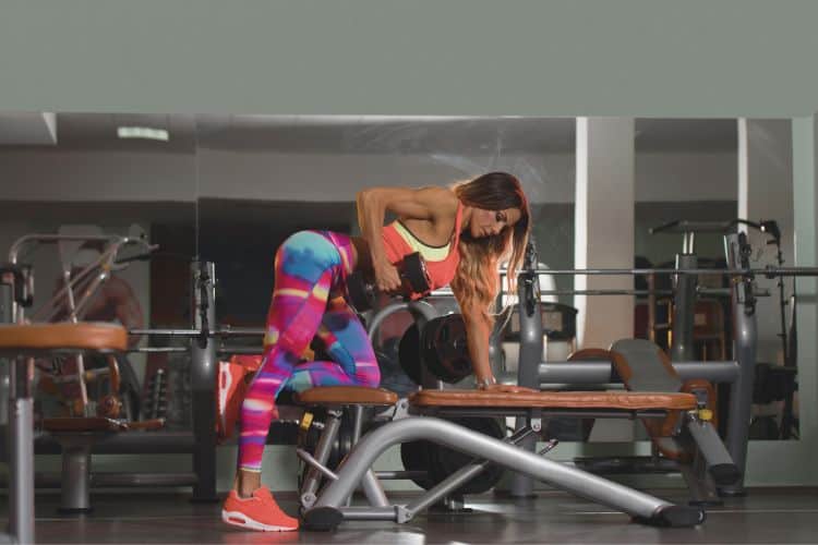 Woman performing perfect dumbbell bent over rows during a 45-minute full body weight loss workout in a gym.
