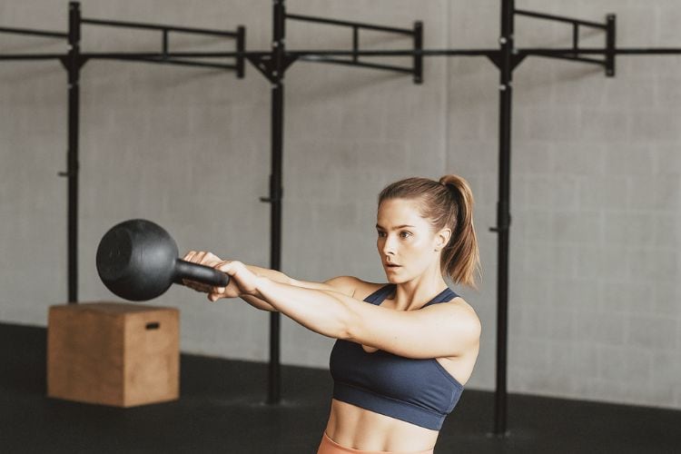 A fit woman performs a kettlebell swing in a CrossFit gym. During a 30-minute CrossFit workout program for women.