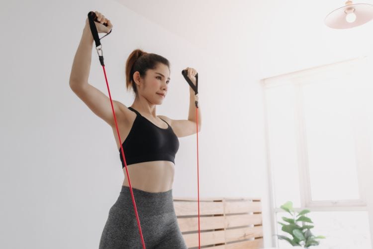 Woman performing resistance band Overhead Shoulder Press in a living room during a 30 minute full body workout