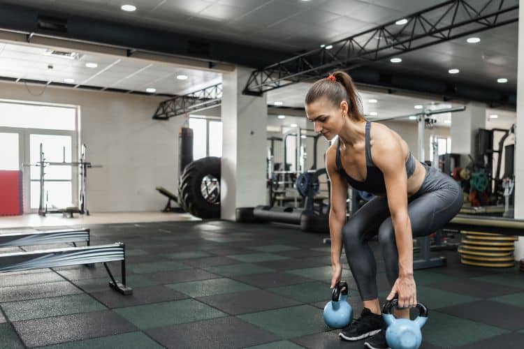 Woman doing bodyweight squats at home during warm up for a 30 minute lower body workout