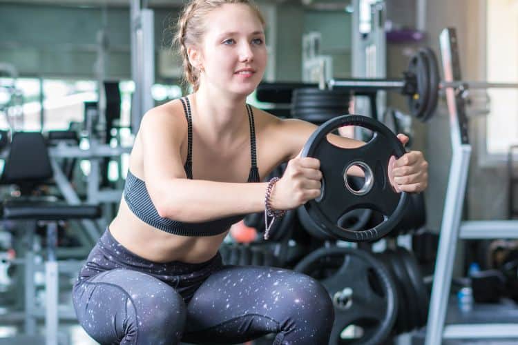 Fitness woman doing full body squat workout with a plate for leg strength