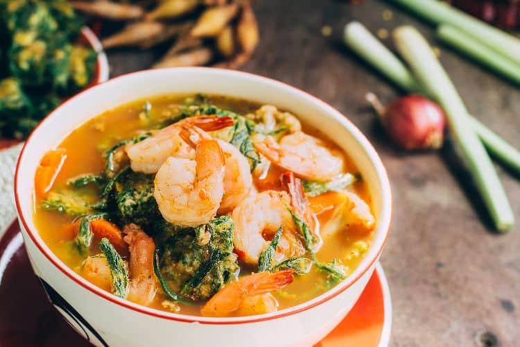 Bowl of Mediterranean fish soup with fresh herbs and lemon wedges