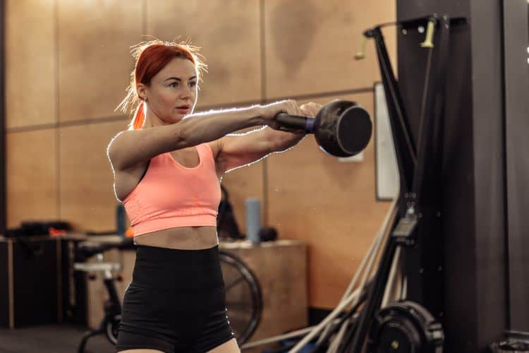 Woman demonstrating proper form for Kettlebell swing, a key move in the 20-minute full body strength training workout.