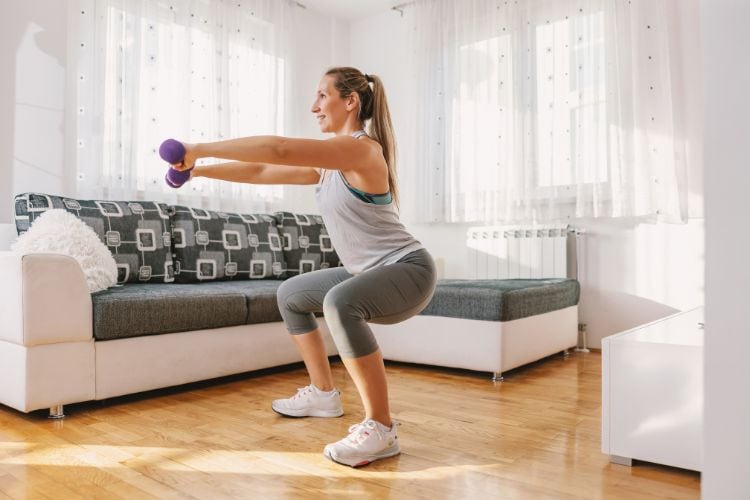 Home workout image of woman going beginner strength training with dumbbells in living room for Women’s Fit Club strength routine