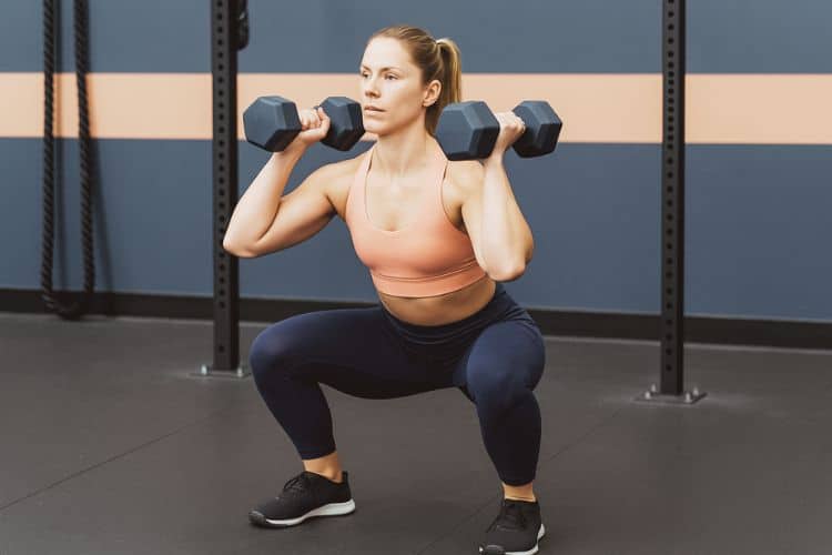 A woman performing a dumbbell thruster during a 30-minute full body EMOM workout at