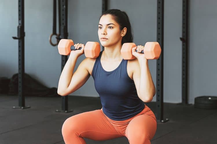 A woman performing a dumbbell front squat in the gym as part of a full-body dumbbell complex workout for women.