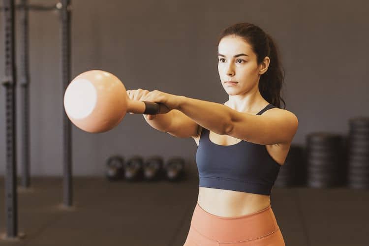 A woman performing a powerful kettlebell swing during a 20-minute full-body kettlebell workout routine.