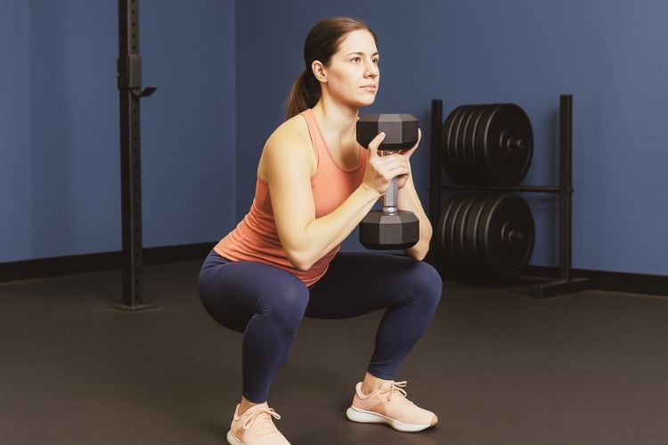 Woman performing a goblet squat with a dumbbell during a 15 minute HIIT leg day workout at the gym.