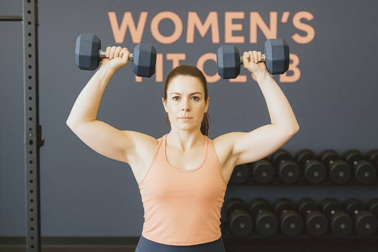 Woman performing dumbbell shoulder press in during 15-minute upper body HIIT workout