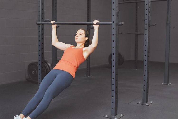 A woman performing a hanging rows for a pull-up bar workout in the gym during a full-body calisthenics pull-up bar workout
