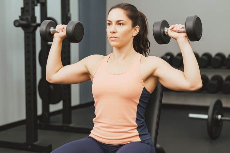 woman performing seated dumbbell Arnold press during 45-minute upper body HIIT dumbbell workout in the gym