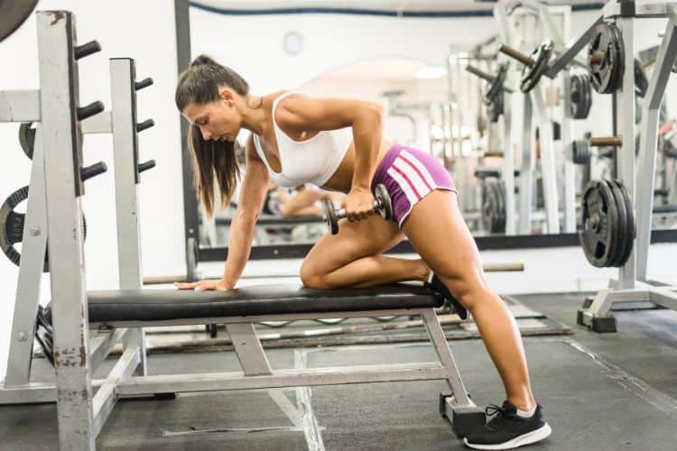 A woman performing a dumbbell bent over row during a 10-minute back dumbbell workout in a gym.