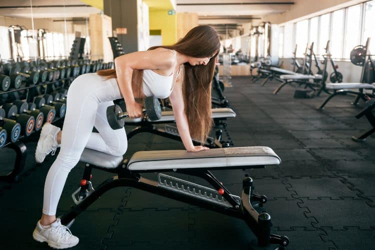 A woman preforming bent over dumbbell row during a10 minute back workout in the gym.