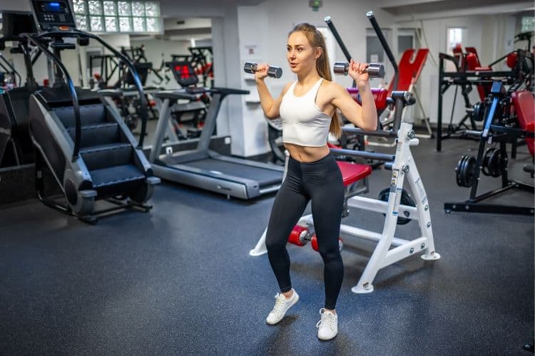A woman beginner smiling and ready to start the 10-minute full body compound workout at the gym.