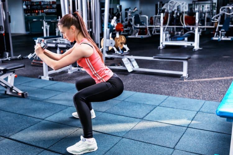 A woman performing dumbbell squat in a 10-minute full body EMOM workout at the gym.