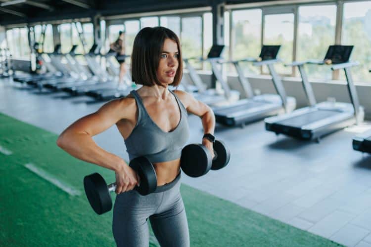 A woman performing dumbbell upright rows during a 15-minute free weights workout in a gym.