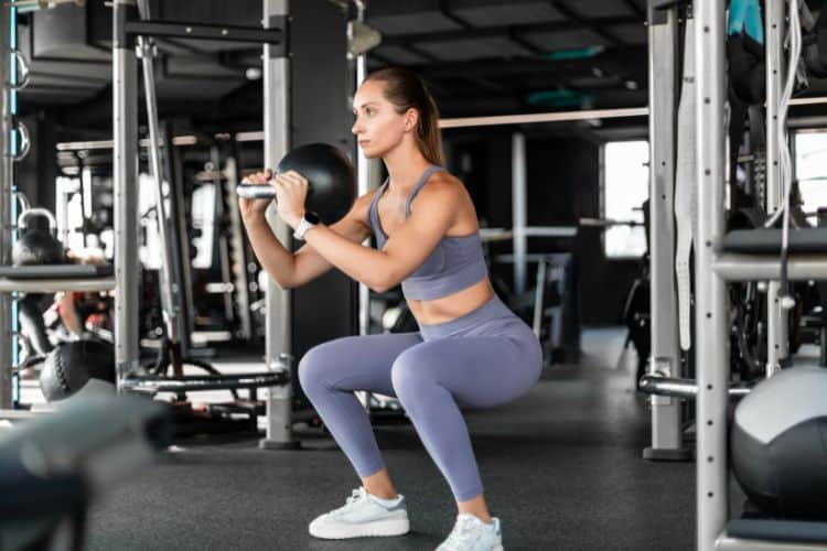 A woman performing goblet squat during a 15 minute full body strength training workout in the gym.