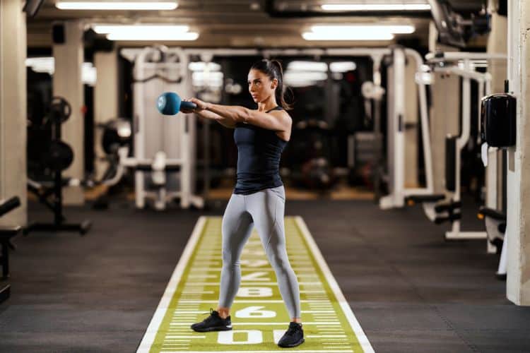 A woman performing kettlebell swing during a 15-minute full body kettlebell workout at a gym.