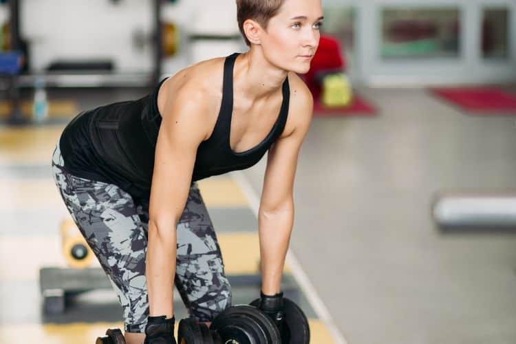 A woman performing a dumbbell deadlift in a 20-minute full body compound workout at a gym.