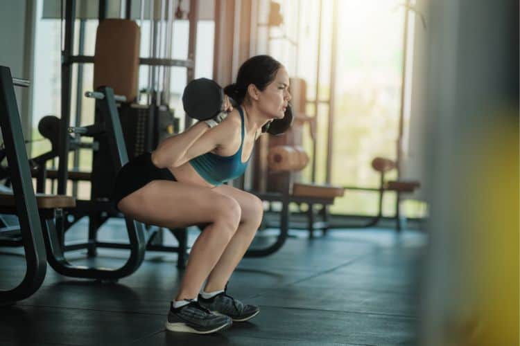 A woman properly performing a barbell squat in a 30 min full body strength training routine in the gym.