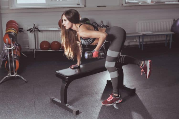 A woman performing a dumbbell bent over row during a 30-minute full body compound workout at a gym.