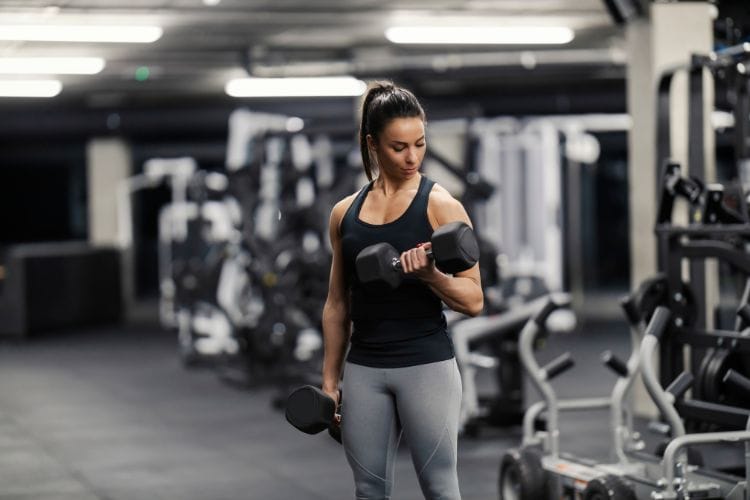 A woman doing dumbbell bicep curls during a 40-min full body dumbbell workout in a gym.