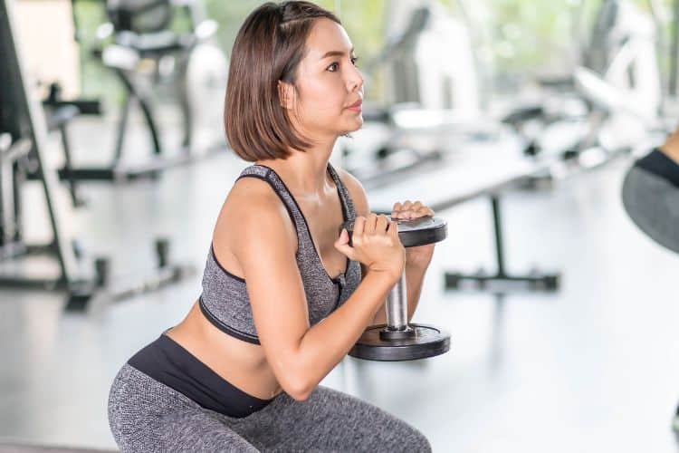 A woman performing a dynamic full body exercise like a dumbbell squat to press in a 45 minute full body cardio and strength workout in a gym.