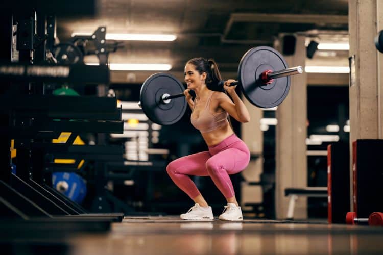 A woman performing a barbell back squat during a 45-minute full body compound workout at a gym.
