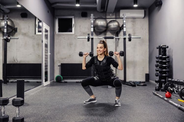 A woman performing a 5 minute full body compound workout with dumbbells weights in a gym.