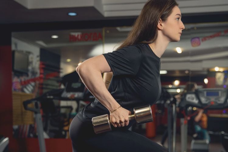 A woman performing a dumbbell thruster in a 5 minute full body dumbbell workout at a gym.