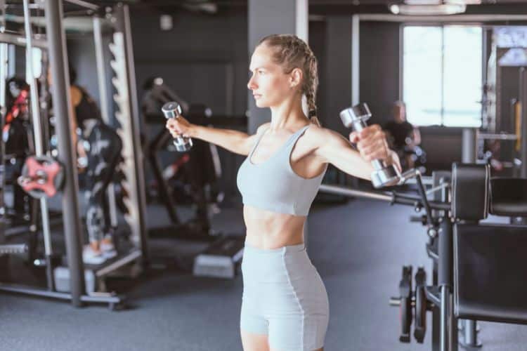 A woman performing Lateral Arm Raises for a 20 minute arm HIIT workout in the gym.