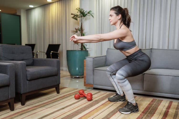 Woman performing a bodyweight squat during a 30 minute full body at-home HIIT workout in her living room.