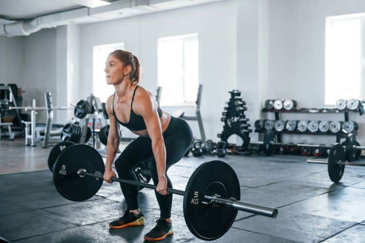 A woman performing a barbell bent-over row during a 30-minute killer barbell back workout routine in a gym.
