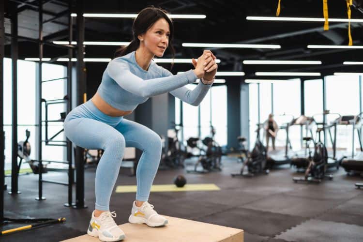 Woman doing bodyweight squat for cardio in a 10-minute full body strength and cardio workout in a gym.