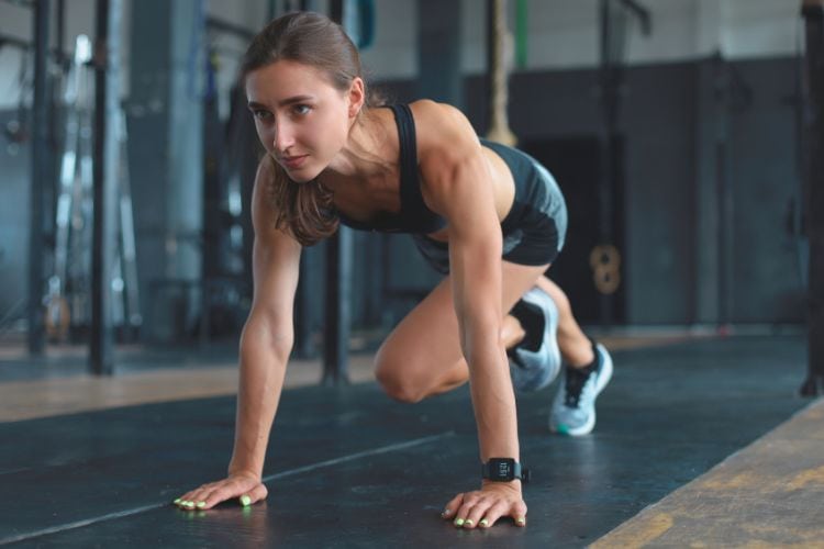 A woman performing a high-intensity mountain climber exercise in a 5-minute full body cardio strength workout at a gym.