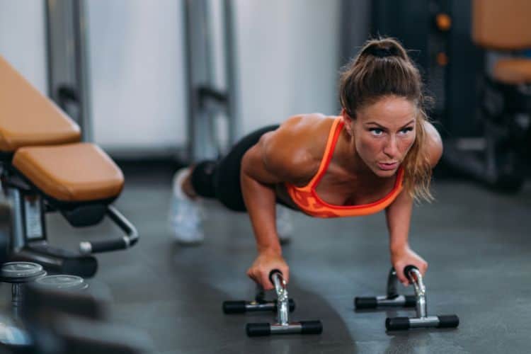 A woman performing a dynamic full body exercise like push-ups during a 15 minute full body cardio strength workout at a gym.