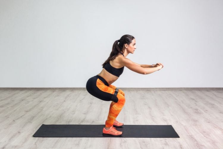 A woman performing a bodyweight squat for 45 minute fat loss circuit workout for beginners in the gym.