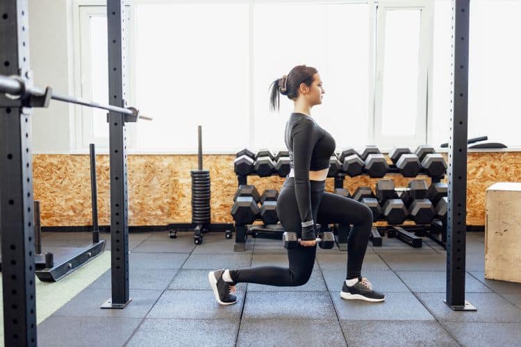 Woman performing a dumbbell reverse lunges during a 25-minute full body dumbbell MetCon workout at a gym.