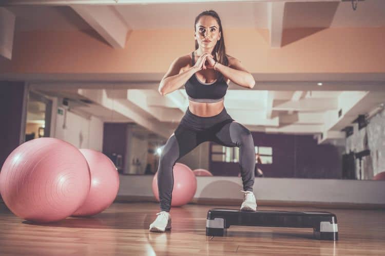 A woman performing a bodyweight squat during a 30-minute HIIT workout for fat loss at the gym.