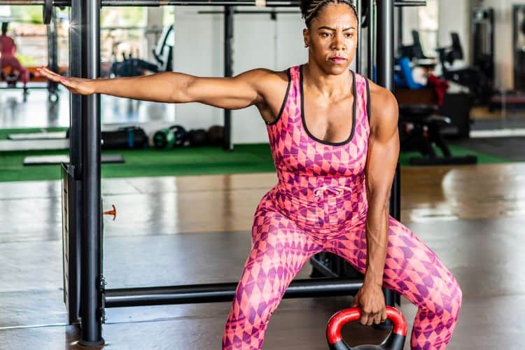 A woman performing a kettlebell single-hand deadlift during a 30-minute fat burning kettlebell workout at the gym.