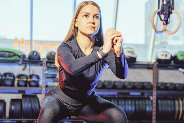 Woman performing bodyweight squats during a 45-minute full body calisthenics circuit workout in the gym.