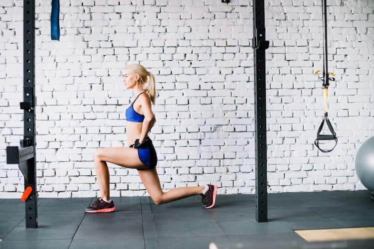 Woman performing a reverse lunges as part of a 15-minute full body calisthenics workout routine in the gym.
