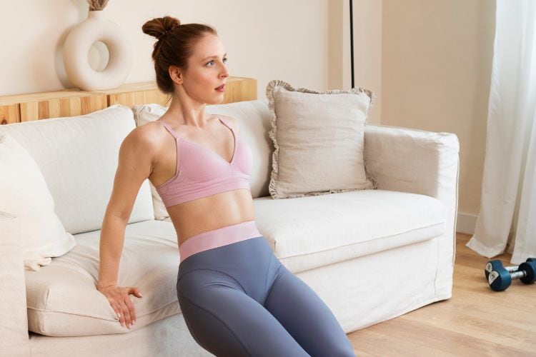 Woman performing triceps dips to strengthen chest and arms in 30-minute HIIT home workout routine.