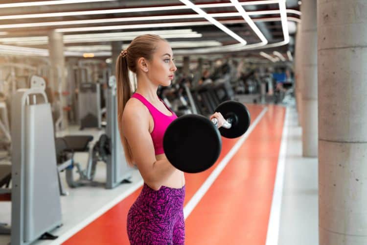 Woman doing alternating biceps curls as part of a 20-minute HIIT biceps workout in the gym.