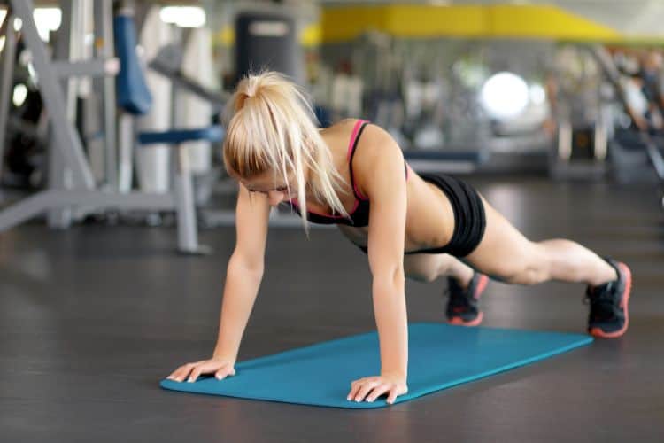 A woman performing a powerful plank jack walks during a 20-minute full-body power HIIT workout in the gym.
