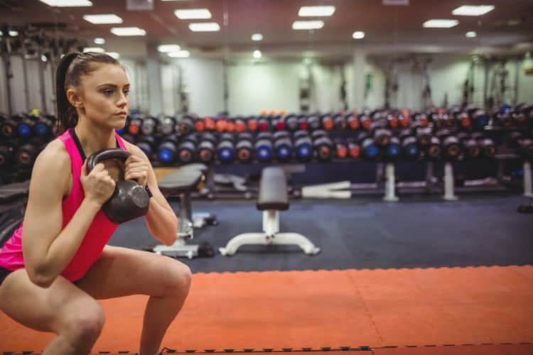A Woman over 40 holding a kettlebell in goblet squat position, demonstrating deep squat form during a 25-minute full body over 40 kettlebell workout in a gym.