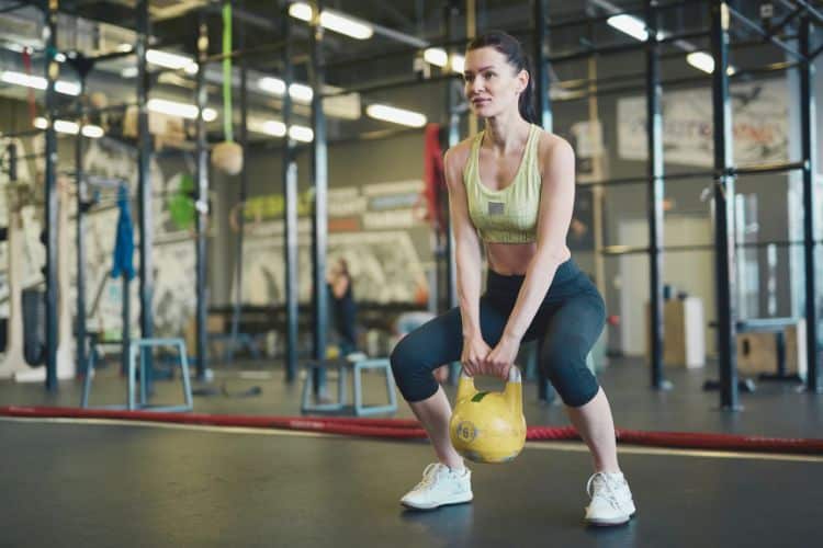 A woman performing kettlebell deadlifts during a 5-minute full body kettlebell workout for woman over 40 in a gym.