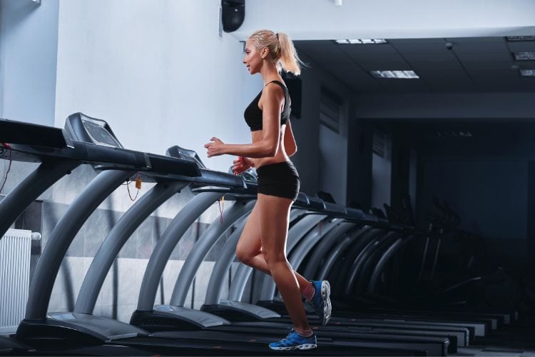 A woman walking briskly on a treadmill during a 30 minute low-impact HIIT treadmill workout in a gym. 