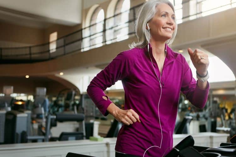 A vibrant, smiling woman in her 50s confidently running on a treadmill at a moderate pace during a 25 minute treadmill workout for over 50 in a gym.