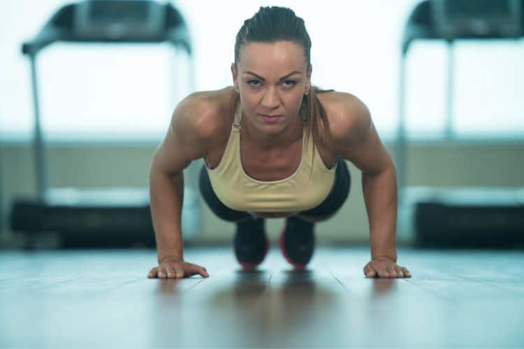A woman performing push ups during 30 minute upper body calisthenics circuit workout in the gym